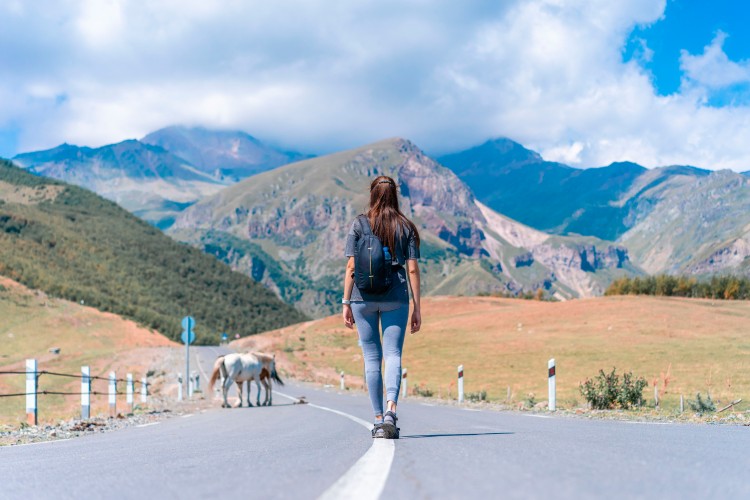 woman-with-backpack-on-the-road-with-mountains-on-background