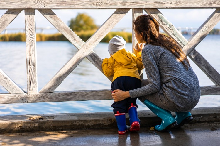 mom-with-a-child-stand-at-a-wooden-fence-and-look-at-the-river