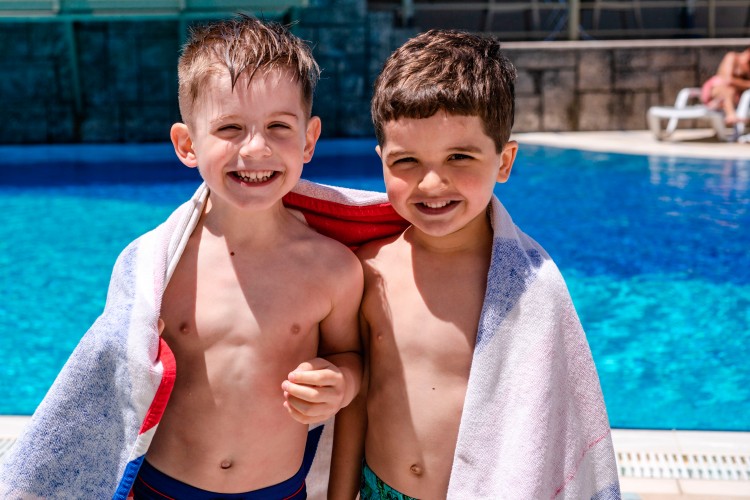 two-smiling-boys-with-towel-near-the-pool