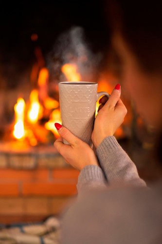 a-cup-of-tea-in-female-hands-against-the-background-of-the-fireplace