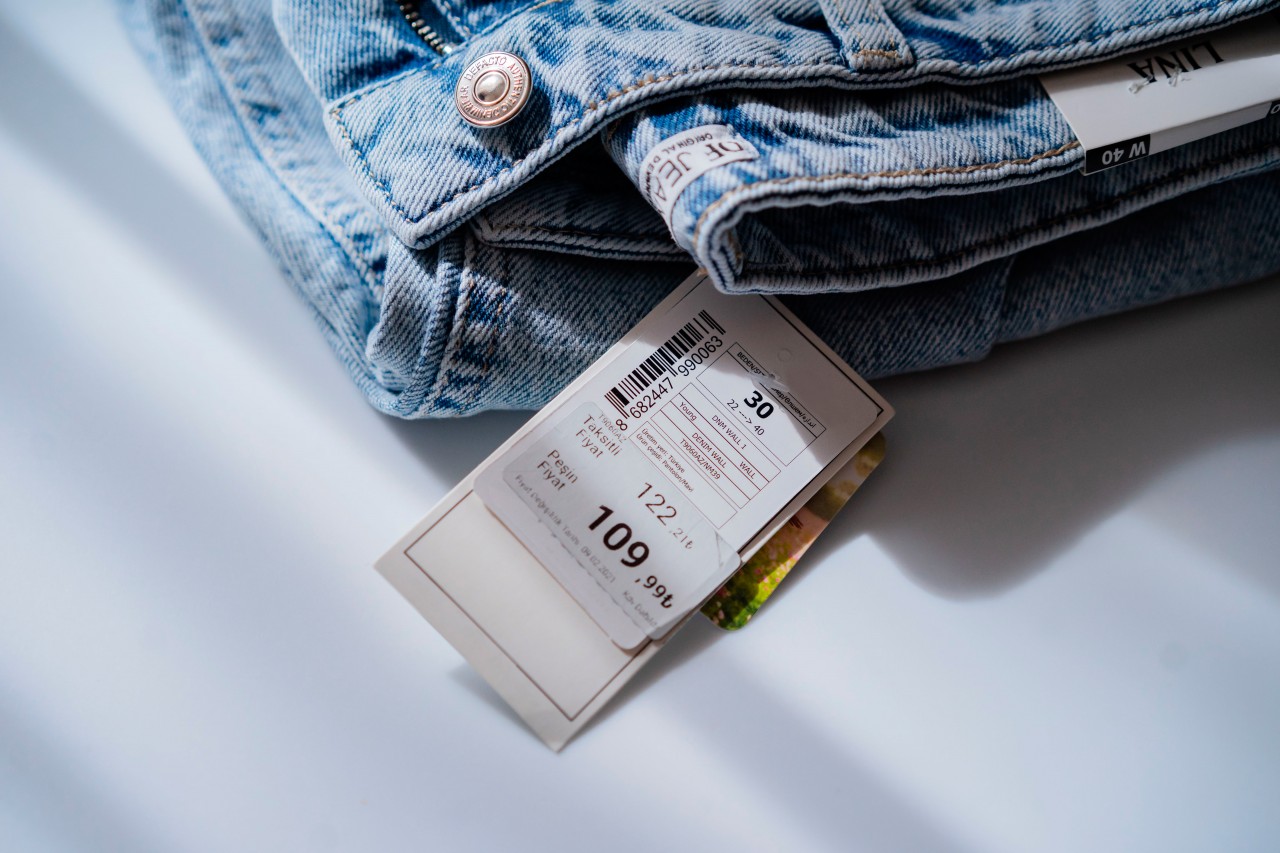 Denim jacket with price tag on light background