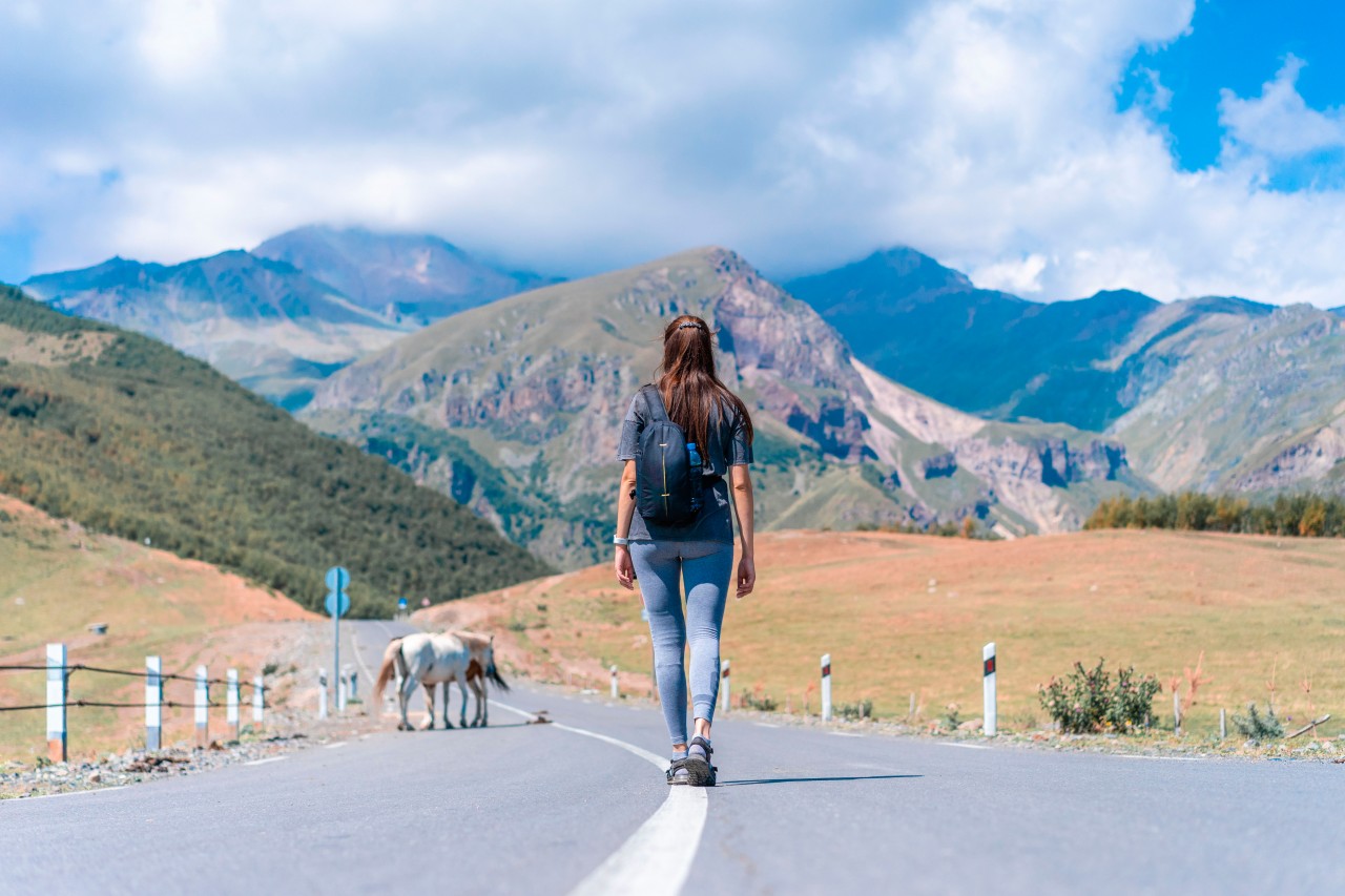 Woman with backpack on the road with mountains on background