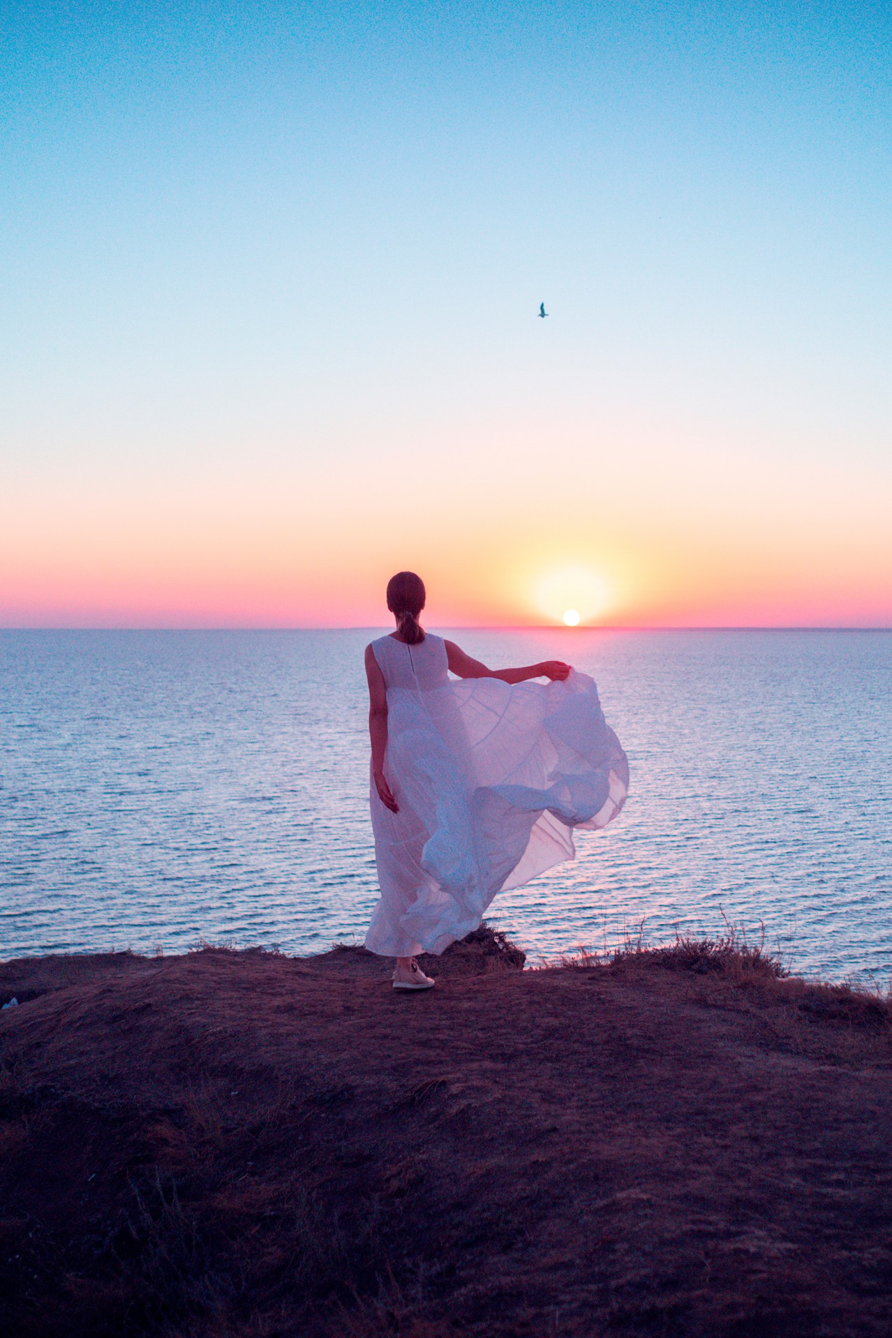 Woman in white dress near sea at the sunset