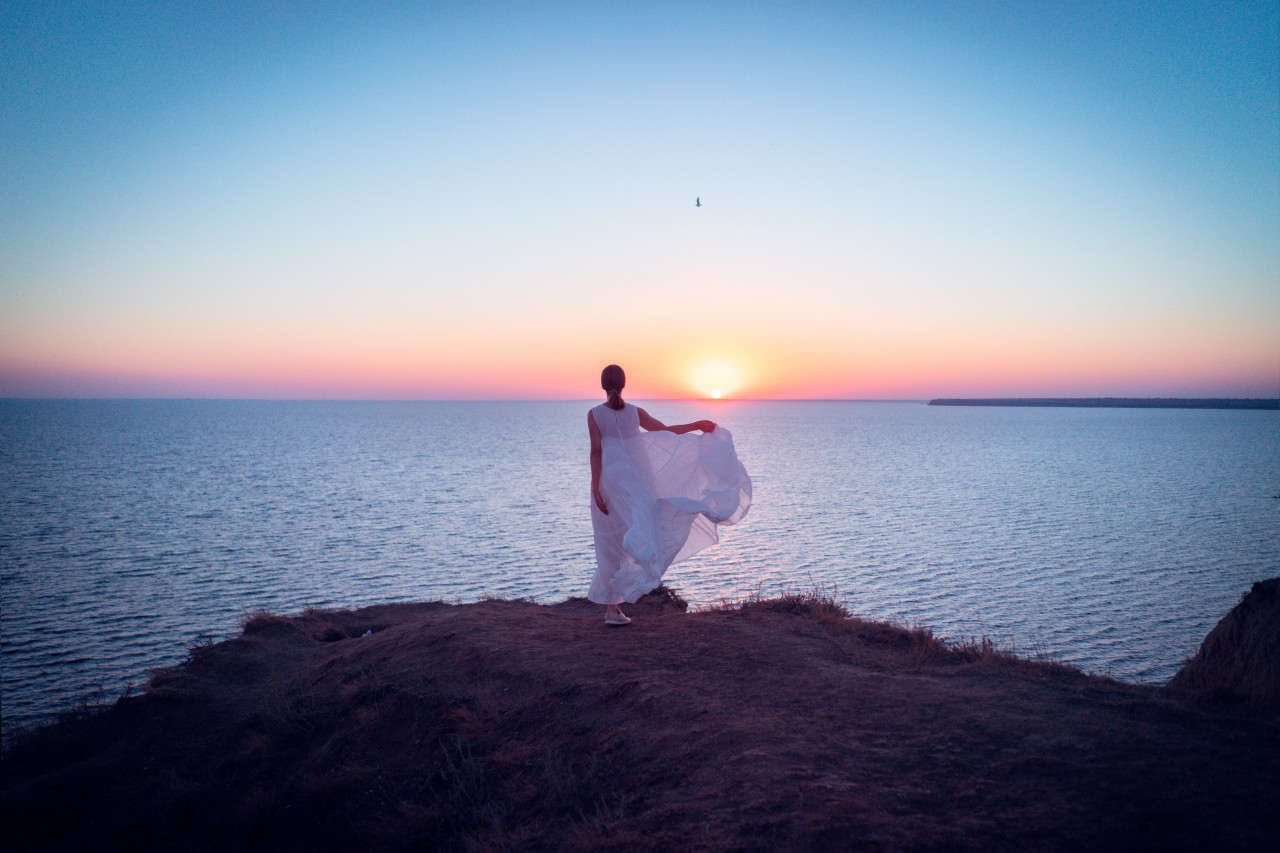 A Young Woman in a White Dress Admires the Sunset