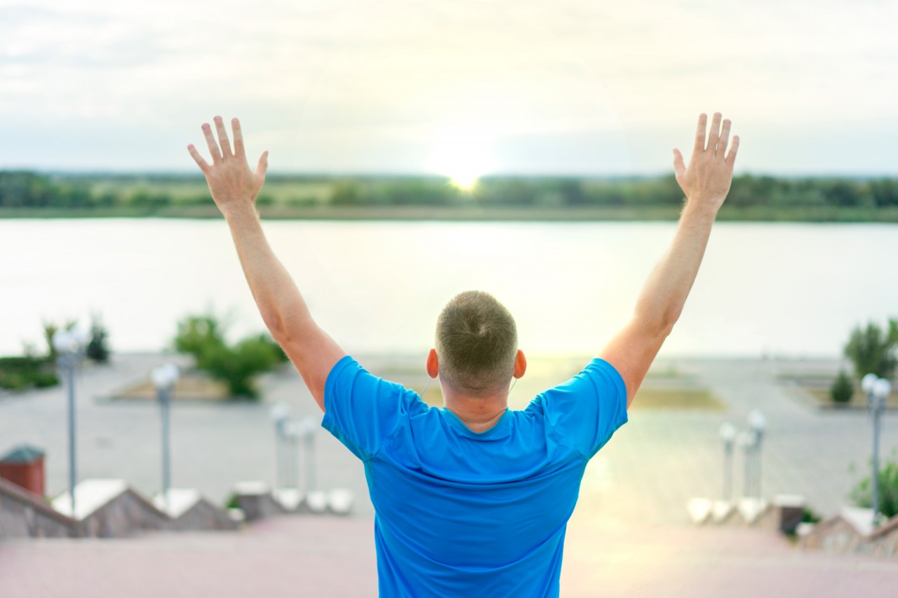 Man in blue t-shirt posing with raised hands on a city background