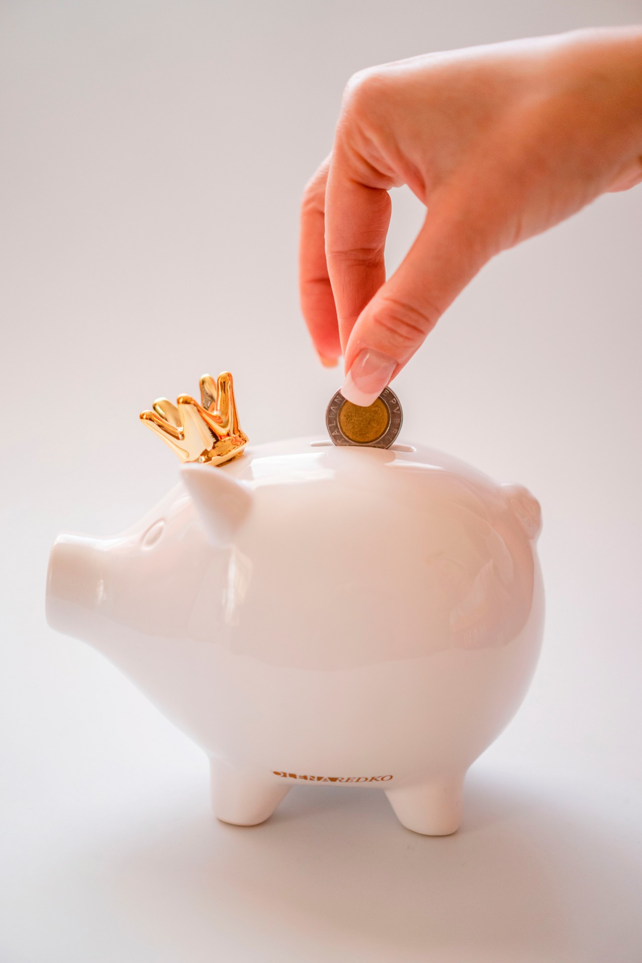 Woman with French manicure putting coin in the piggybank
