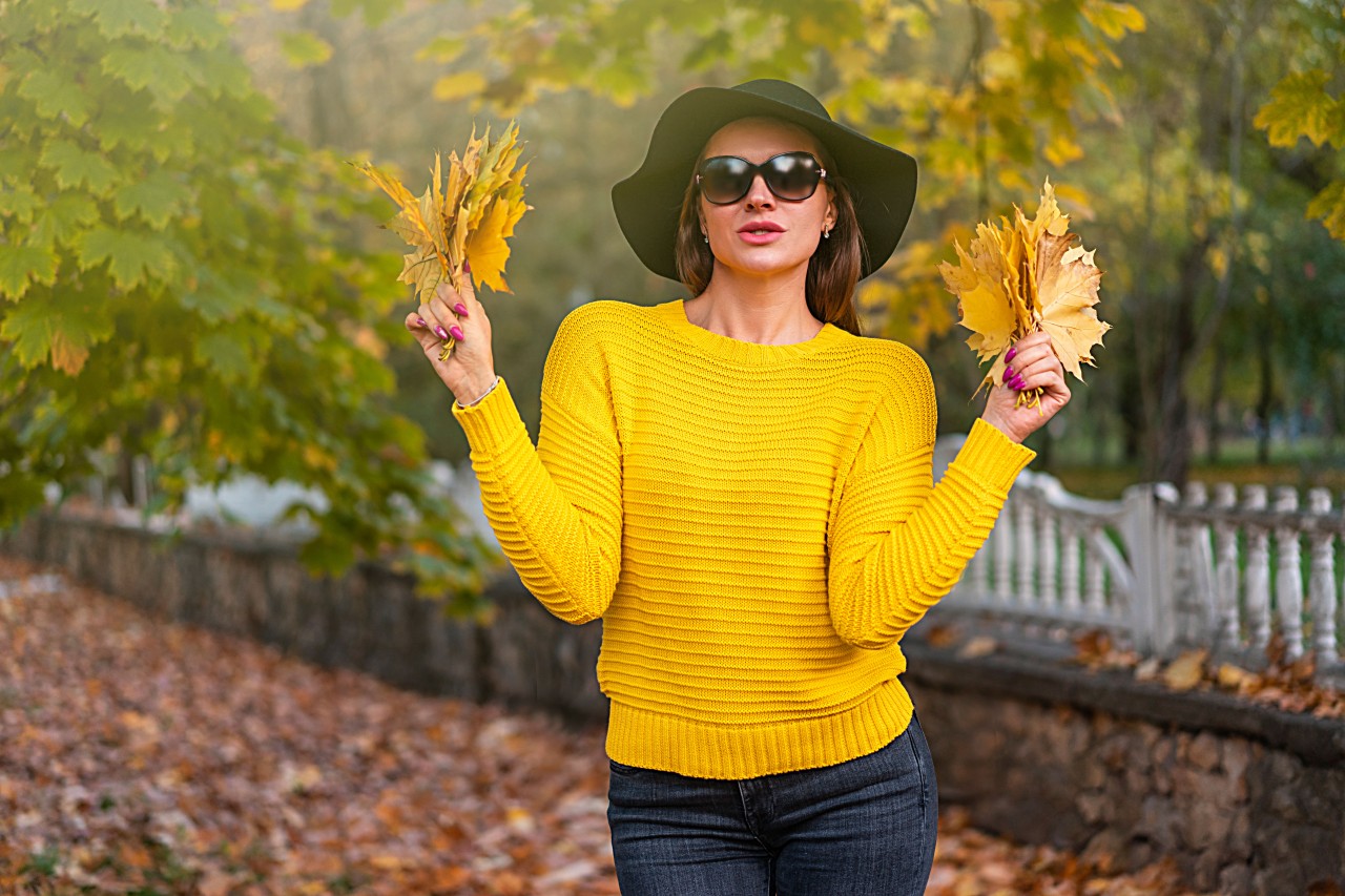 Young Brunette Woman in a Black Hat on a Background of Autumn Trees