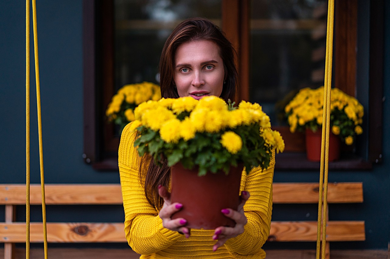   A young brunette woman in a yellow sweater with a bouquet of flowers 