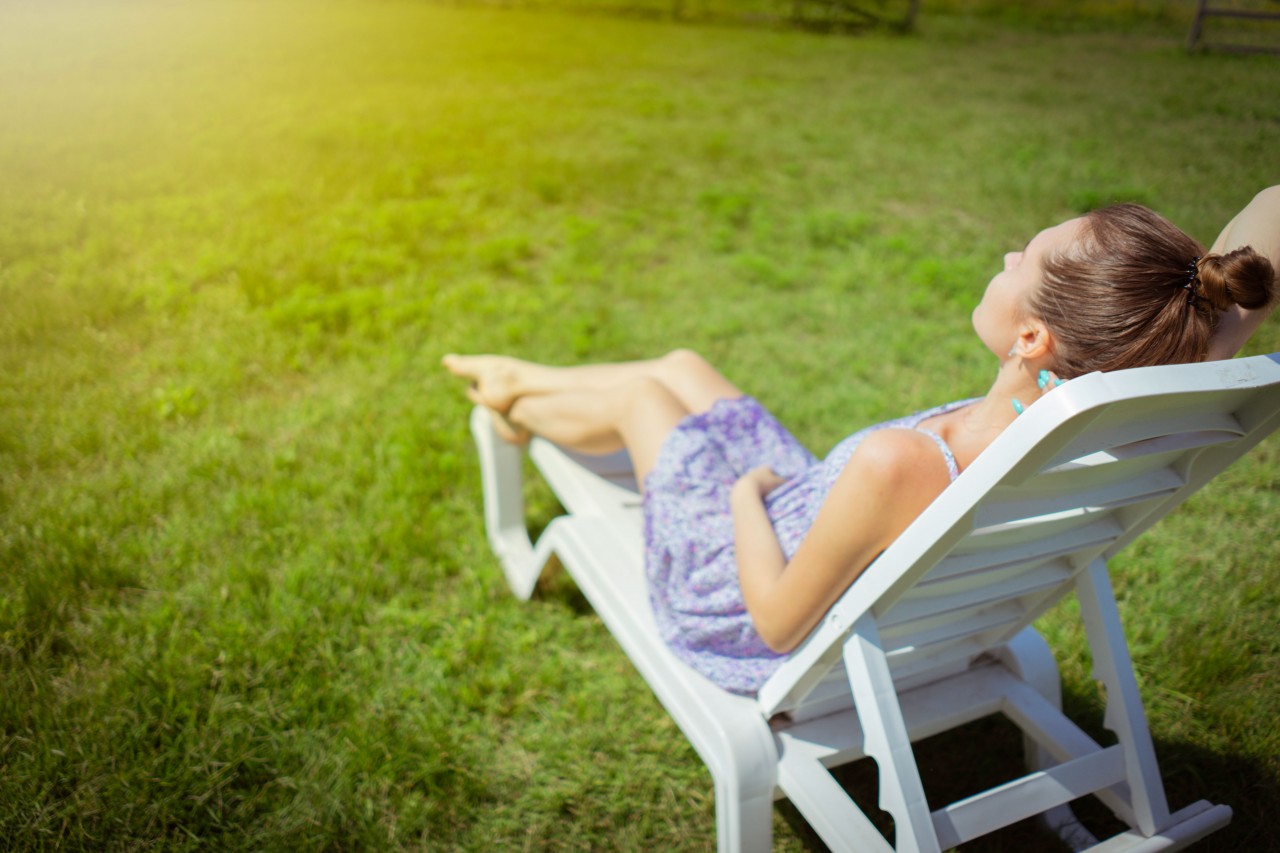 Young Woman on a Deck Chair on a Background of Green Grass 