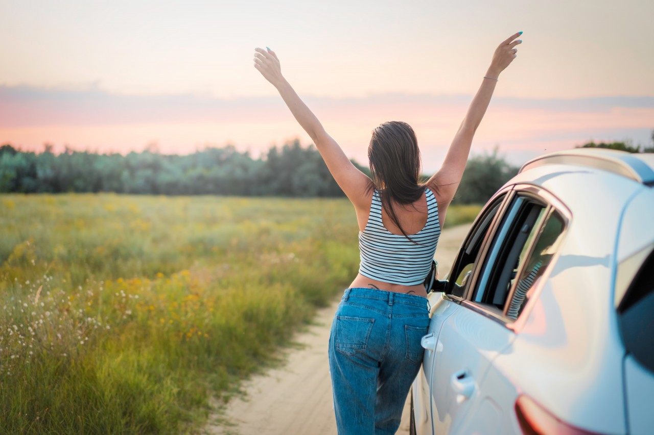 Woman standing near car with raised hands