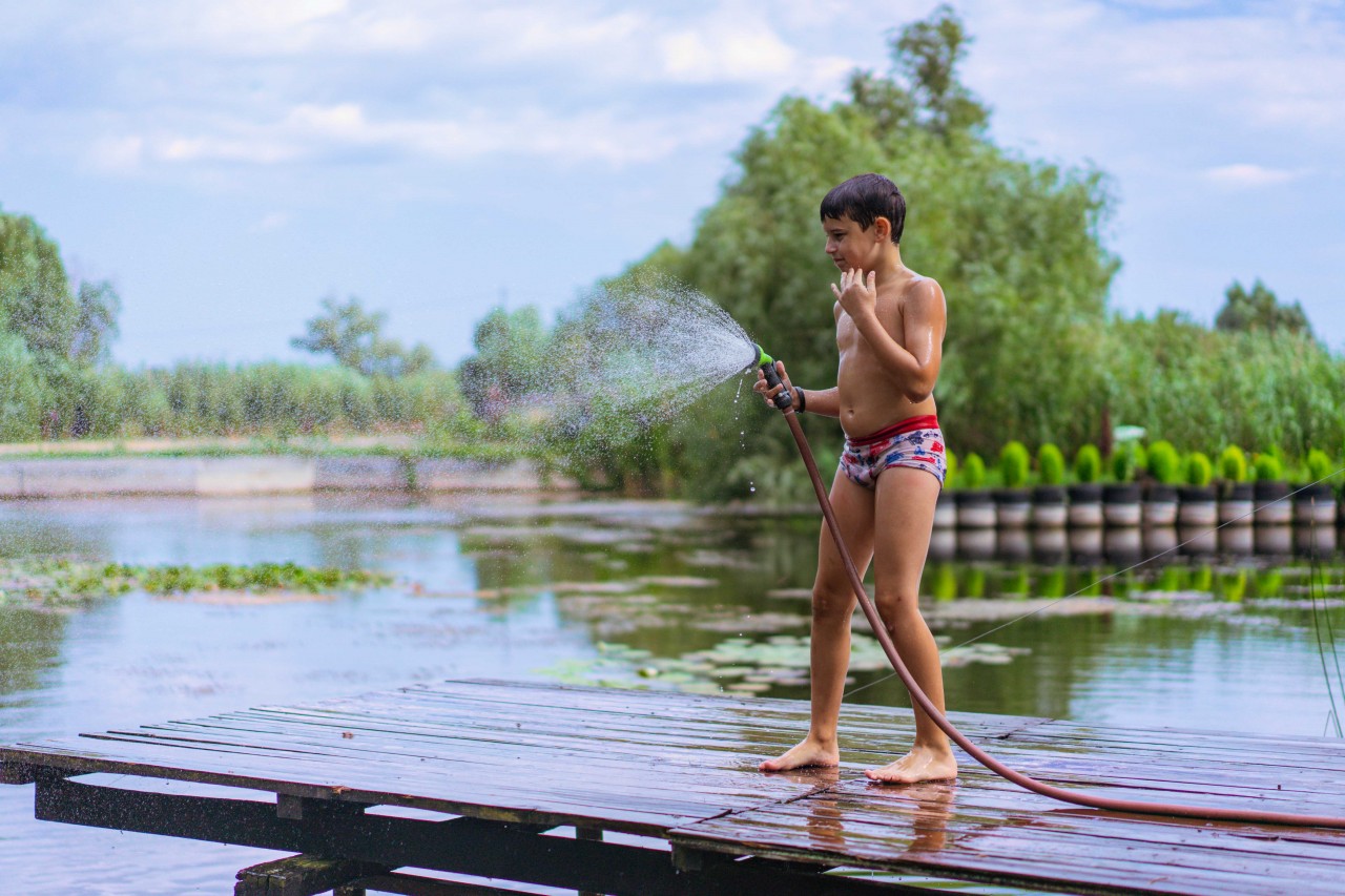 A Young Guy on a Wooden Bridge with Hose for Watering