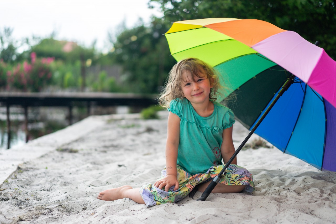 Little girl sitting under umbrella at the beach