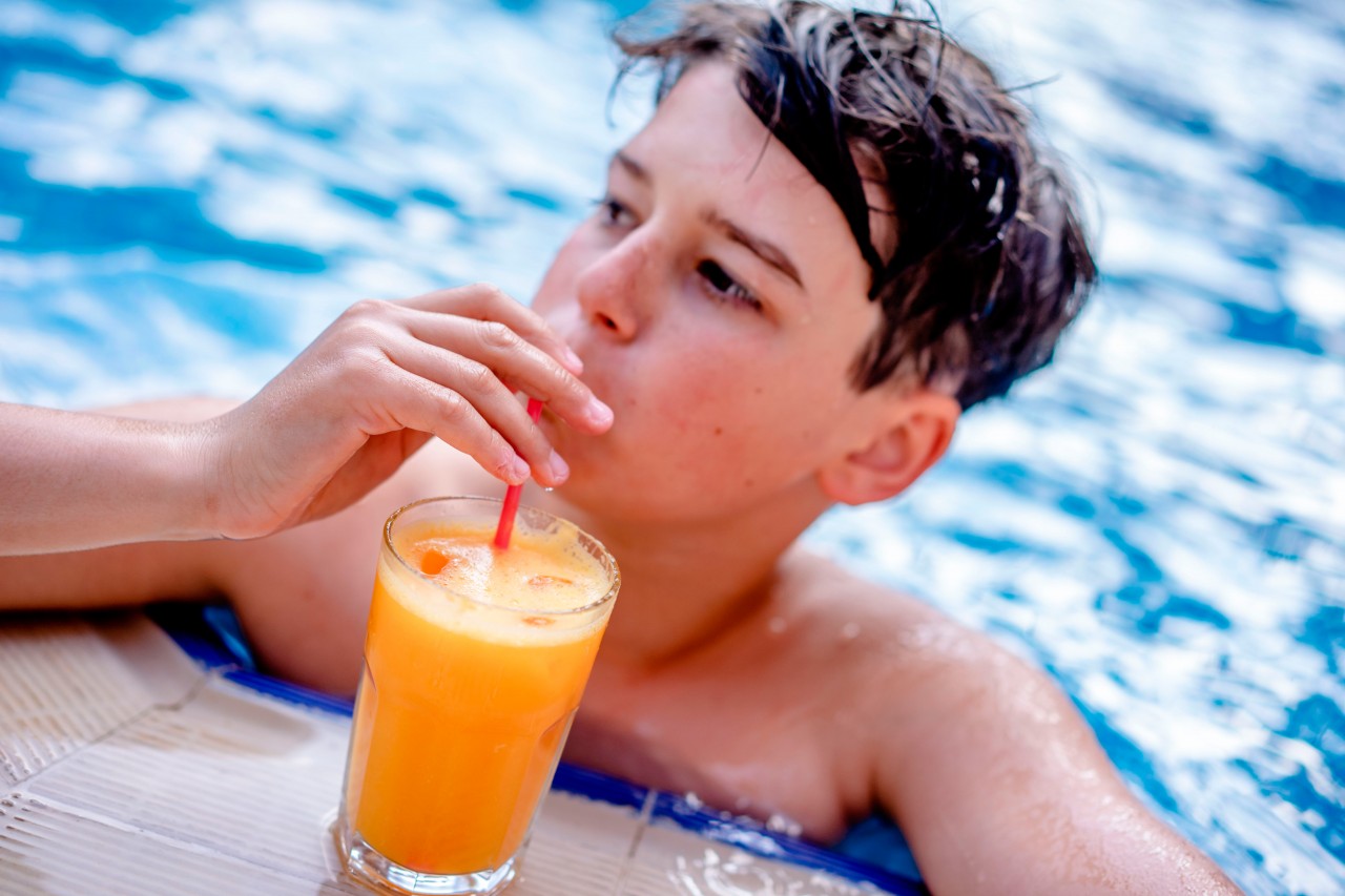 Boy drinking juice in the swimming pool