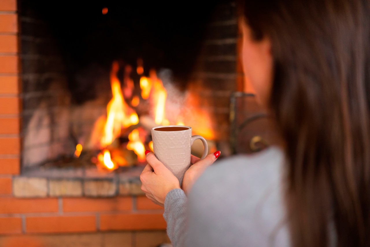 Beautiful Woman with a Cup in Hands by the Fireplace