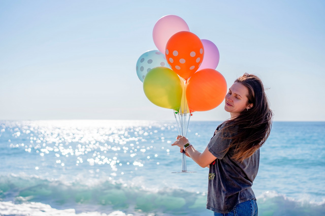 Smiling woman holding party balloons on sea background