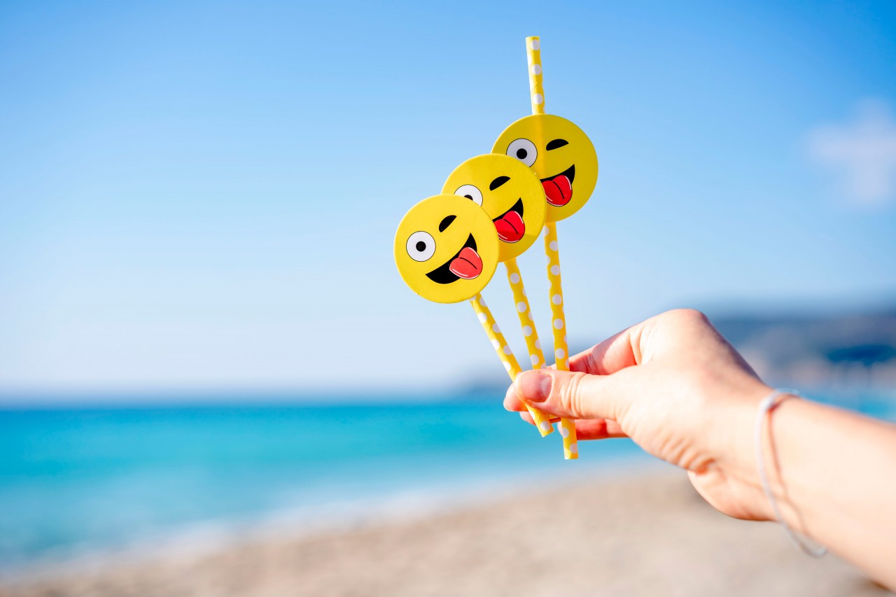 Yellow beverage straws with emojis at the beach