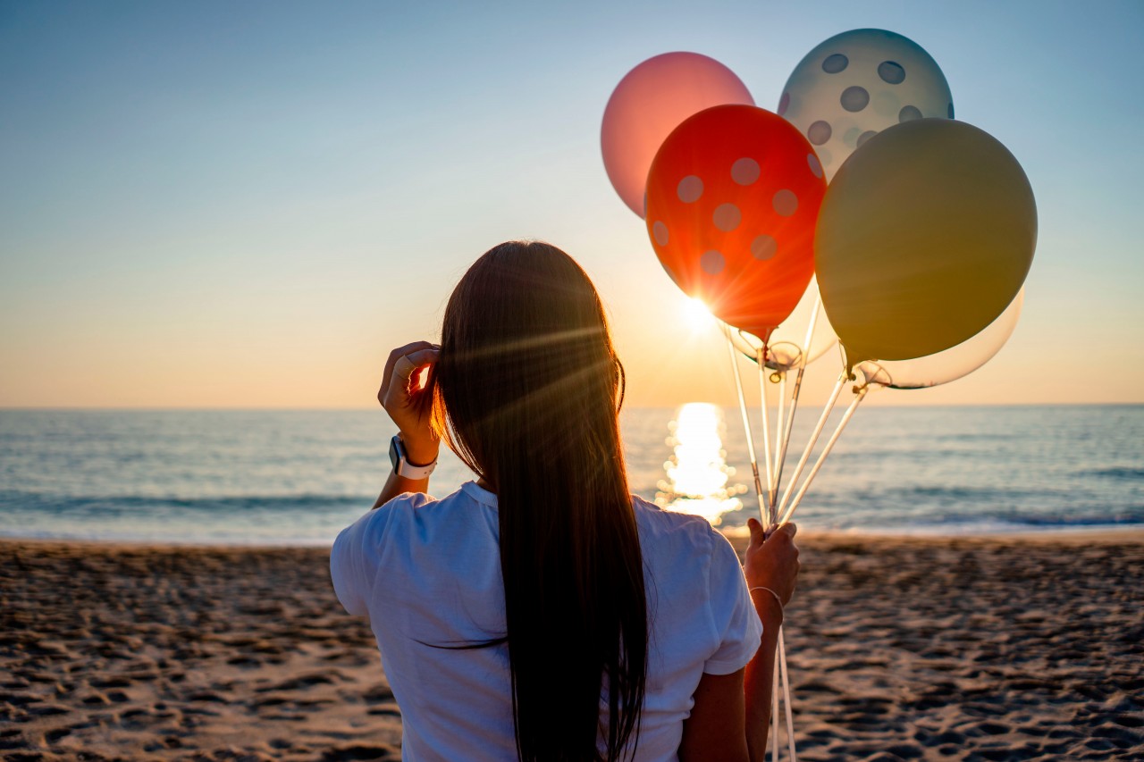 Brunette woman with balloons posing at the beach on sunset