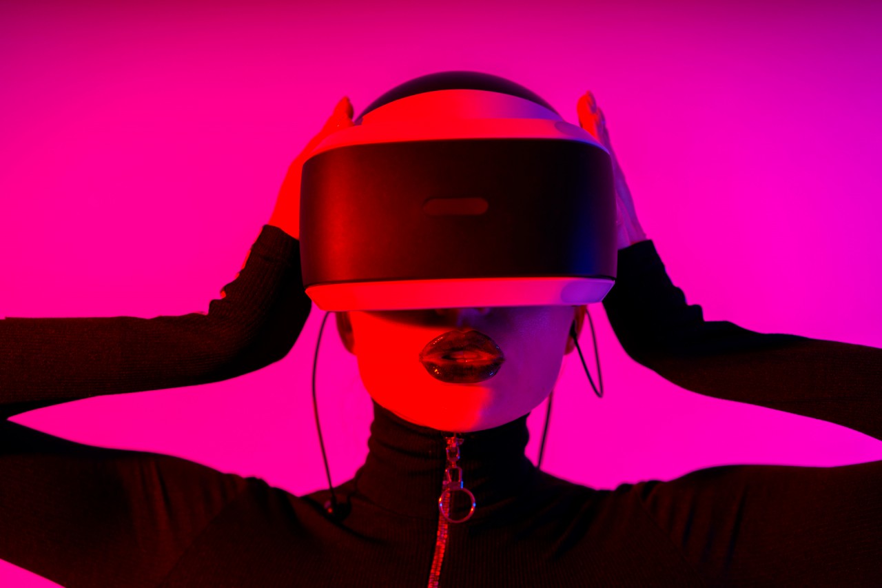 Young woman in VR headset posing on pink background